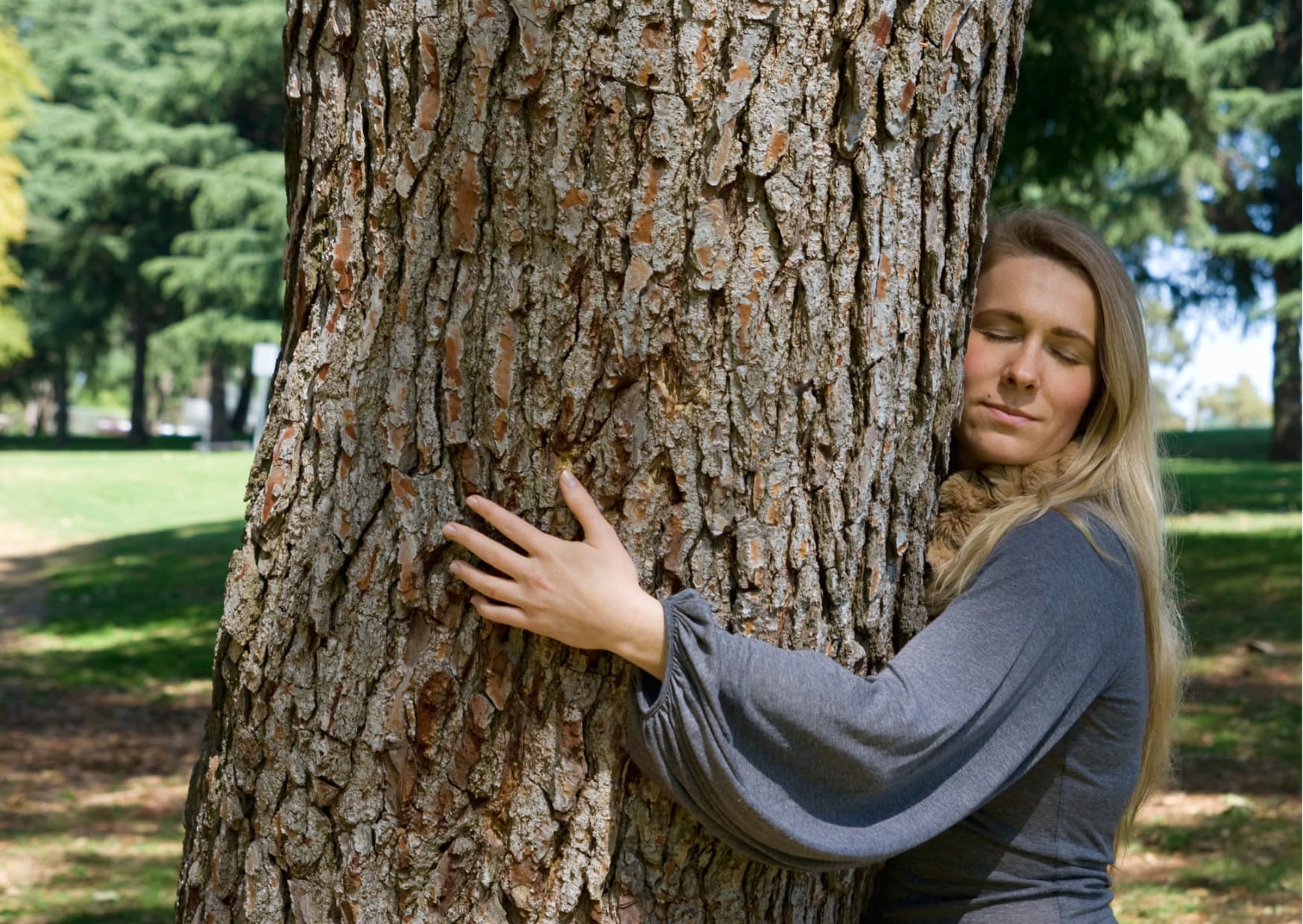Kobieta obejmuje drzewo, przytula się do niego odczuwając radość i spokój