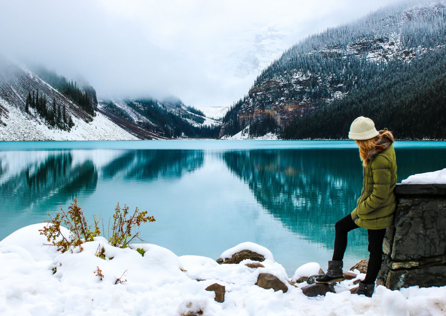 Kobieta stoi nad górskim jeziorem w śniegu