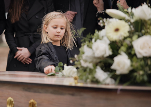 Dziewczynka kładzie kwiaty na trumnie w czasie pogrzebu